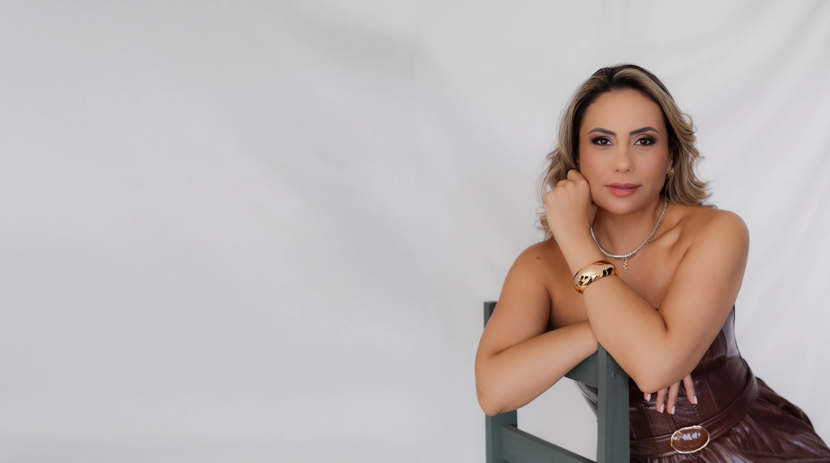 Dra. Márcia Viscardi, fundadora da Reference Odontologia, de vestido marrom, apoiada em uma cadeira em estúdio